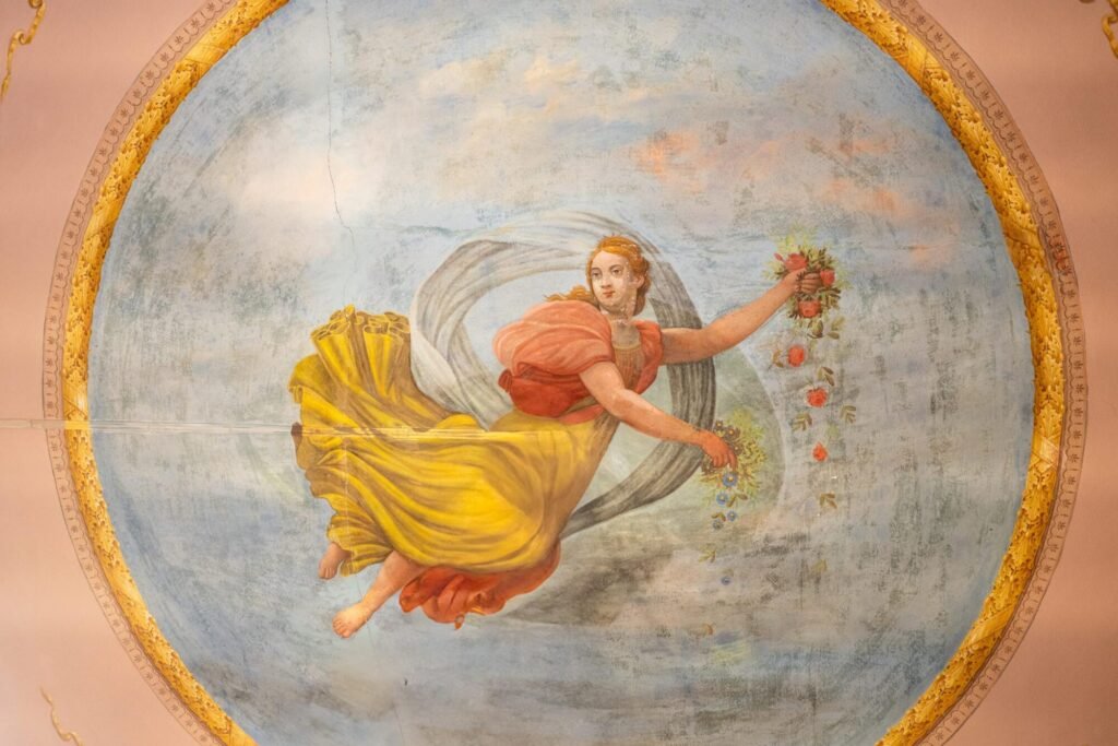 Affresco antico al Palazzo Trecci Tombesi, Montepulciano, raffigurante figura classica con ghirlanda floreale.