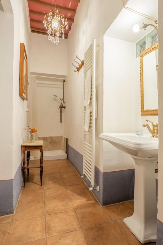 Elegant bathroom with vintage chandelier, antique table, and modern fixtures at Palazzo Trecci Tombesi, Montepulciano.