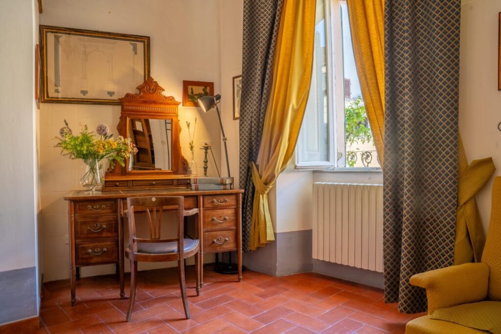 Arredamento elegante in legno con specchio, fiori freschi e tende in una stanza di Palazzo Trecci Tombesi, Montepulciano.