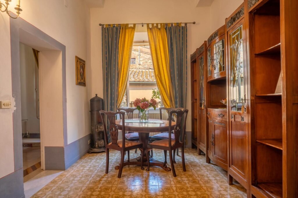 Sala da pranzo elegante nel Palazzo Trecci Tombesi con mobili in legno e vista su tetti toscani.