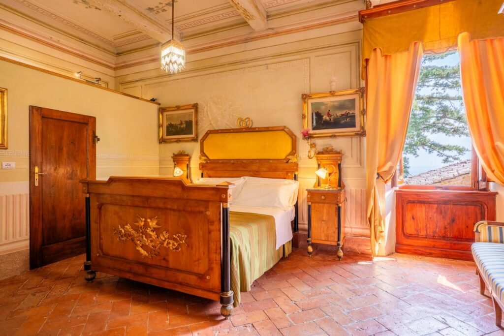 Elegant room with vintage wooden bed, luxurious decor, and large window in Palazzo Trecci Tombesi, Montepulciano.