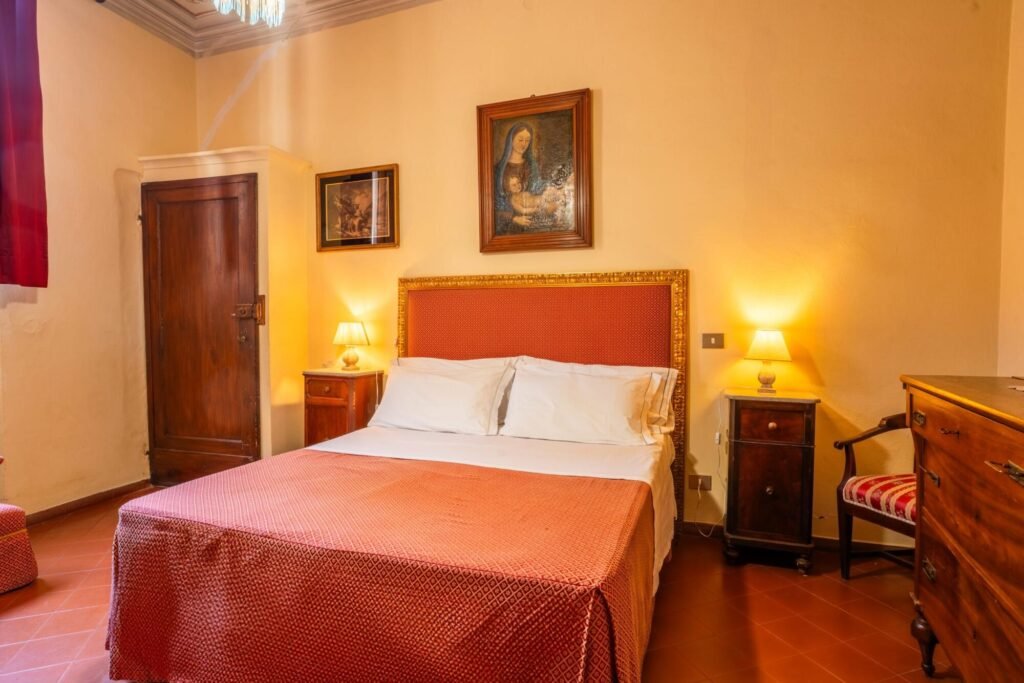 Camera elegante in stile toscano con letto matrimoniale, armadi antichi e illuminazione soffusa a Palazzo Trecci Tombesi.