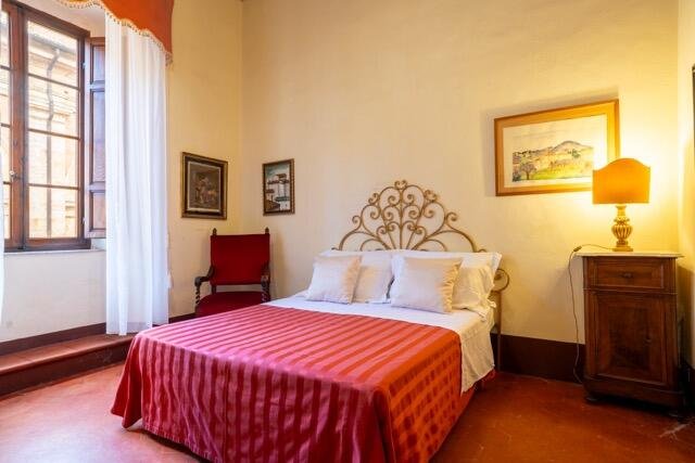 Camera elegante a Palazzo Danesi con letto matrimoniale, decorazioni artigianali, e luce naturale a Montepulciano.