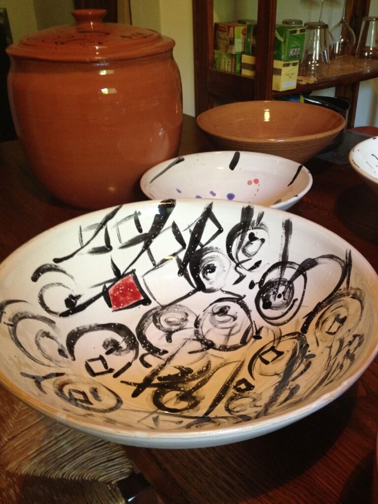 Ceramica artigianale toscana su tavolo di legno, Montepulciano, decorazioni nere e rosse, stile autentico.